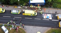 Aerial view of a double-decker bus in a river, surrounded by emergency responders and bystanders.