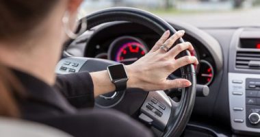 Woman driving a car view from inside of the car and using a smart watch.