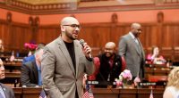 State Rep. Raghib Allie-Brennan speaking at a podium.