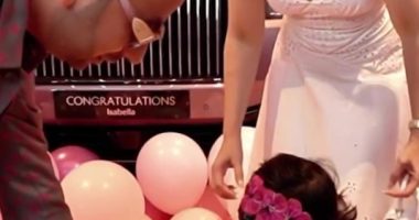 A toddler girl receives a car key from her parents in front of a pink Rolls Royce.