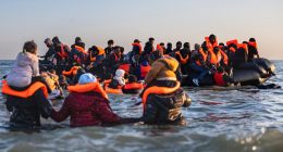 Migrants in life vests board a small boat in the water.