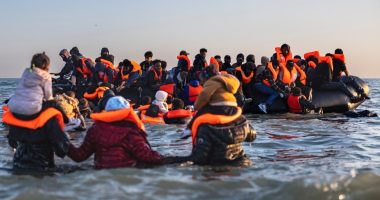 Migrants in life vests board a small boat in the water.