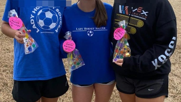 Three girls holding birthday treats, one wearing a Lady Hornet Soccer sweatshirt.