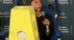 Girl holding microphone, wearing a yellow foam block costume.