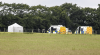 Crime scene with police vehicles and a tent in a field.