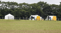 Crime scene with police vehicles and a tent in a field.