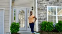 A woman stands in front of her house, which has a new fence that was allegedly installed by her HOA without permission.
