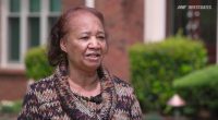 A woman speaks outside her home.