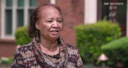 A woman speaks outside her home.