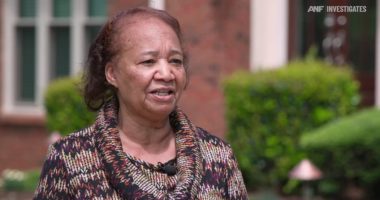 A woman speaks outside her home.
