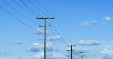 Power lines against a blue sky with fluffy clouds.
