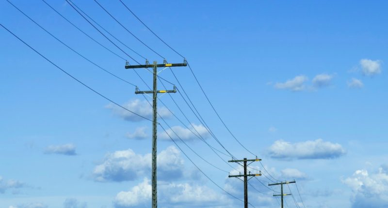Power lines against a blue sky with fluffy clouds.
