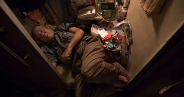 Elderly man sleeping in a small, cluttered room.