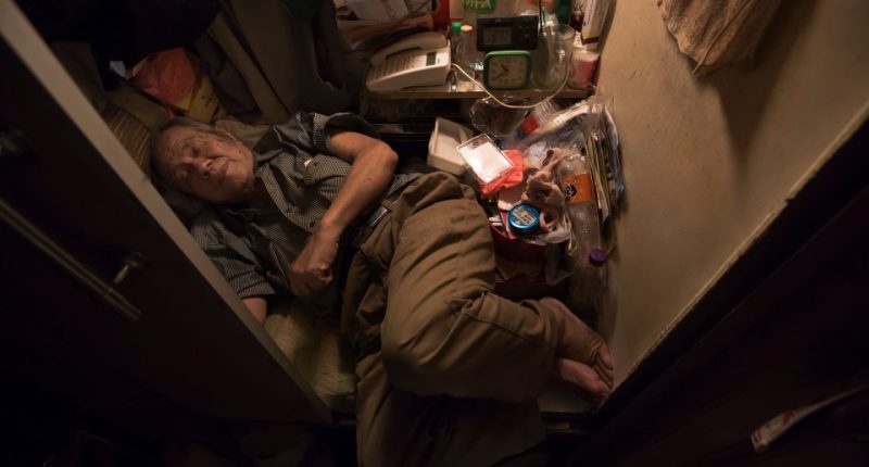 Elderly man sleeping in a small, cluttered room.