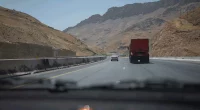 cars drive on highway through arid mountains