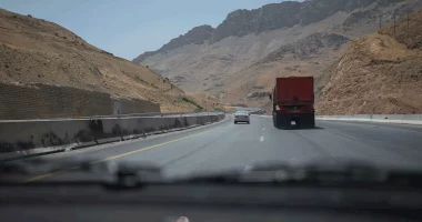 cars drive on highway through arid mountains