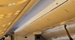 Airplane passenger stowing luggage in overhead bin.