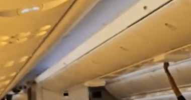 Airplane passenger stowing luggage in overhead bin.
