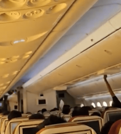 Airplane passenger stowing luggage in overhead bin.