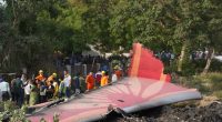 Debris of a crashed airplane with people standing nearby.