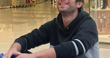 A smiling man sitting on a blue bumper car in a shopping mall.