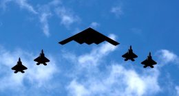 B-2 Spirit bomber flanked by four F-22 Raptor fighter jets.