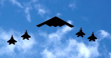 B-2 Spirit bomber flanked by four F-22 Raptor fighter jets.