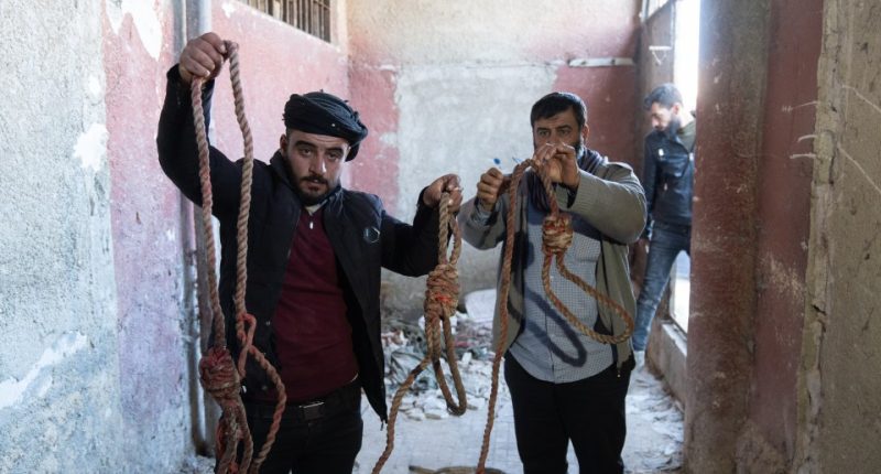 Two men holding bloody ropes in a damaged building.
