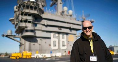 Man in sunglasses standing on the deck of an aircraft carrier.
