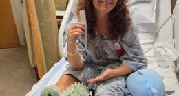 Young woman in hospital gown holding beach umbrella pole that impaled her.