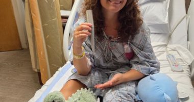 Young woman in hospital gown holding beach umbrella pole that impaled her.
