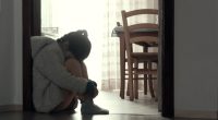A sad young girl sits on the floor hugging her knees.