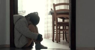 A sad young girl sits on the floor hugging her knees.