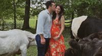 Pregnant woman in orange dress being kissed by a man, with cattle nearby.