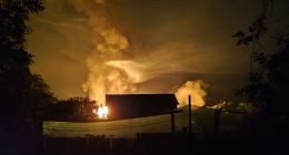 Nighttime view of a large fire burning near a building.