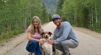 Couple and dog posing on a road in a mountainous area.