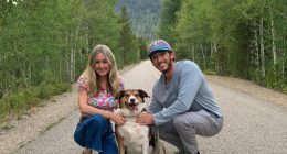 Couple and dog posing on a road in a mountainous area.