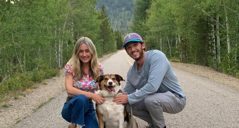 Couple and dog posing on a road in a mountainous area.