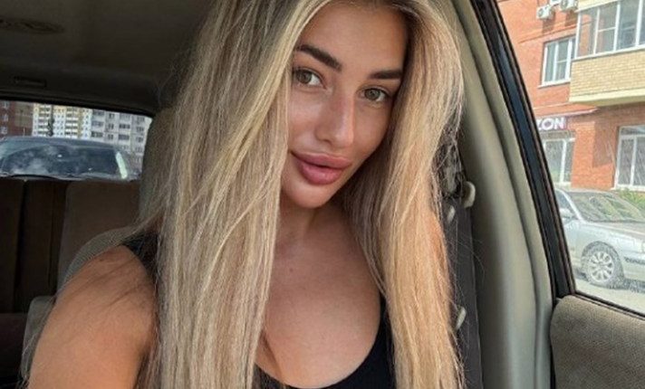 Photo of a young woman with long blonde hair sitting in a car.