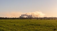 Chemical plant emitting smoke over a grassy field.