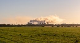 Chemical plant emitting smoke over a grassy field.