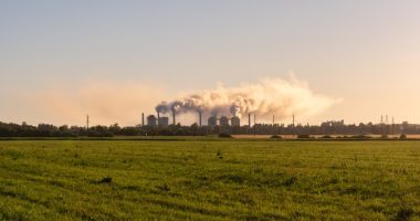 Chemical plant emitting smoke over a grassy field.