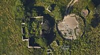 Aerial view of overgrown ruins of a barn and farmhouse.
