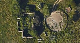 Aerial view of overgrown ruins of a barn and farmhouse.