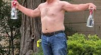 Shirtless man holding two bottles.