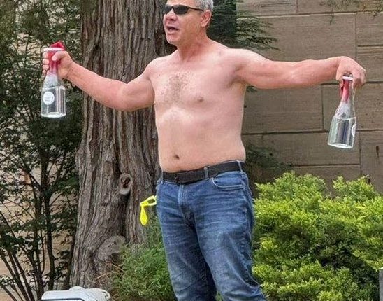 Shirtless man holding two bottles.