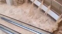 Floodwaters rushing through a shopping mall, submerging escalators.