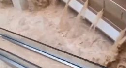Floodwaters rushing through a shopping mall, submerging escalators.