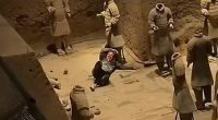 A person sitting among damaged terracotta army statues.