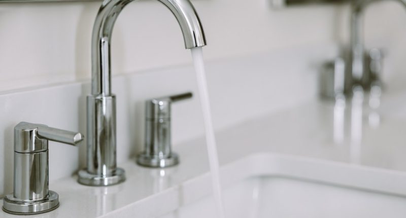 Close-up of water running from a bathroom sink faucet.